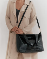 Person holding a large handbag with a crossbody strap, wearing a coat.