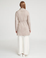 Woman standing, viewed from the back, wearing a coat and trousers.