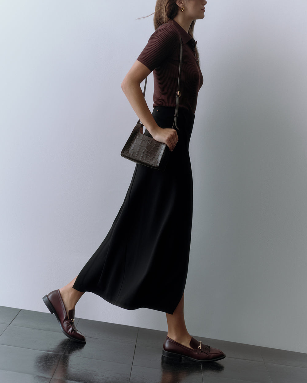 Person walking with a croc-embossed leather handbag wearing a skirt and loafers.