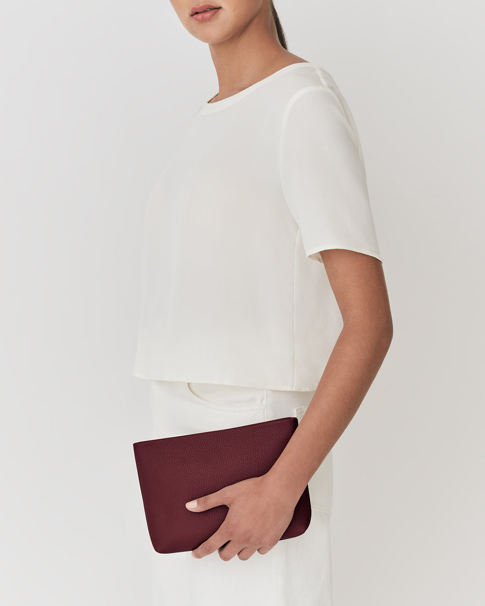 Woman holding a clutch bag, dressed in a short-sleeve top and pants.