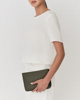 Person holding a small clutch bag under their arm, wearing a short sleeve top and skirt.