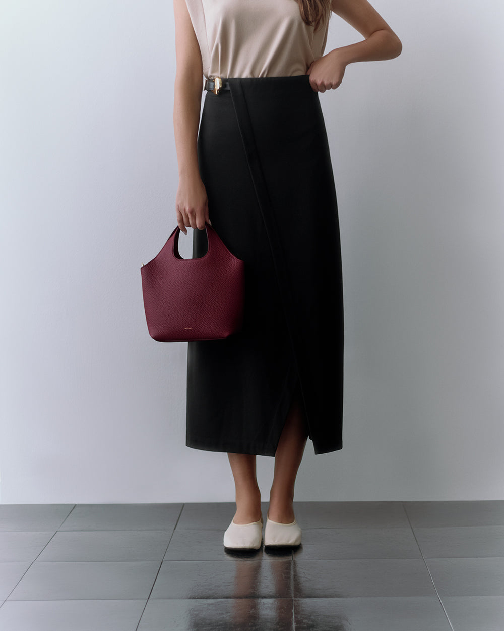 Mini System Tote Person with sleeveless top, long skirt, holding a small handbag, standing on a tiled floor