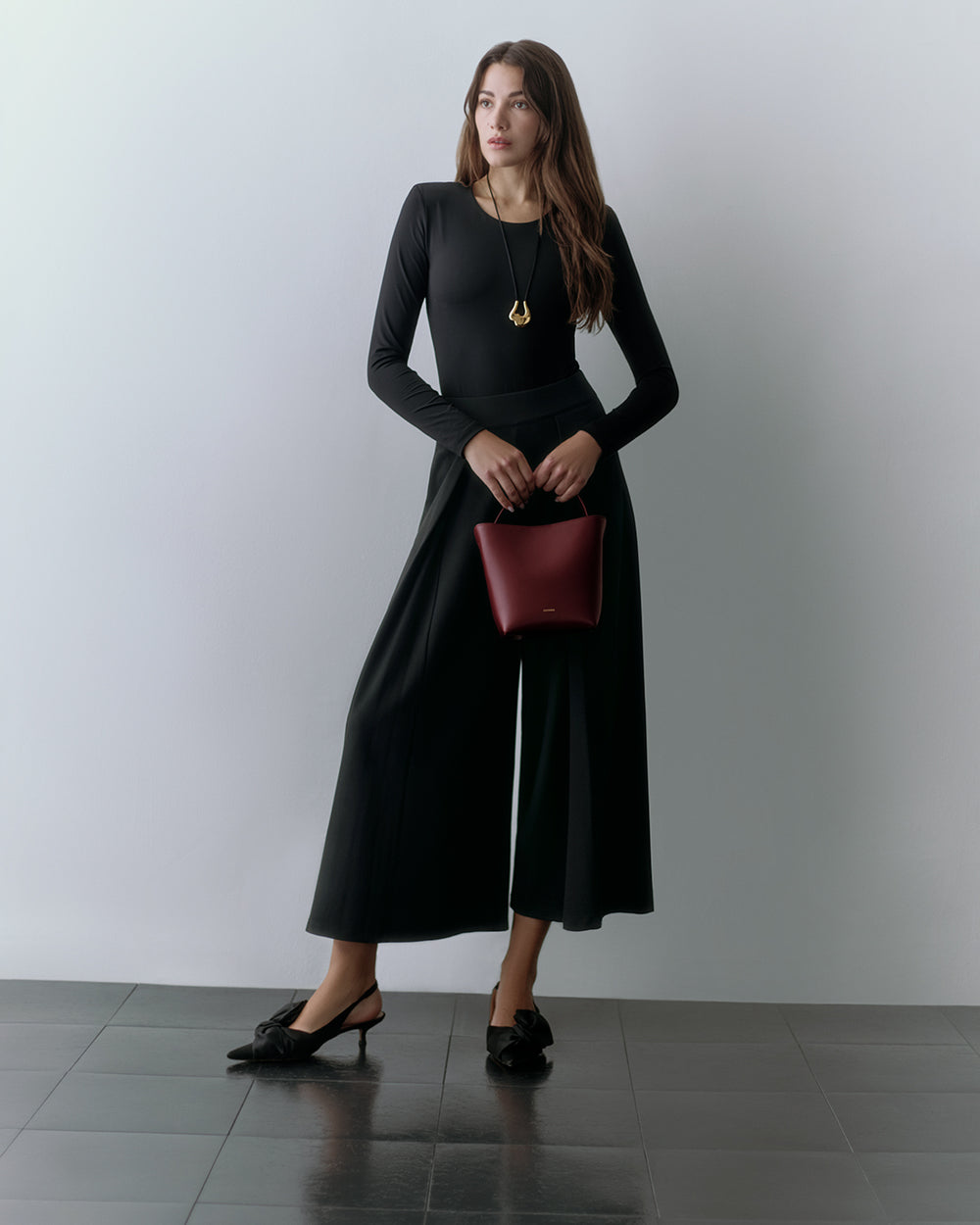 Ponte Pleated Pant Woman wearing a long-sleeve top, wide-leg pants, and holding a small handbag.