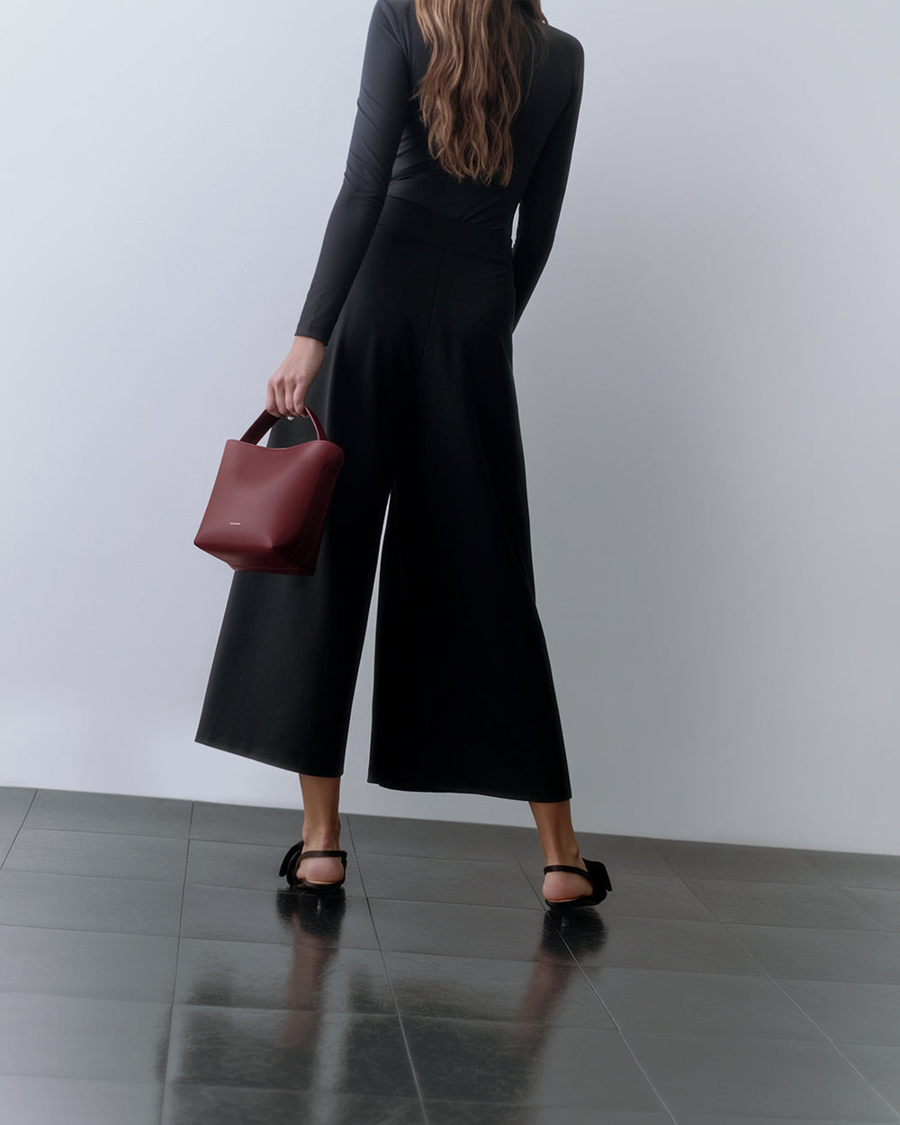 Ponte Pleated Pant Person holding a purse, wearing wide-leg pants and backless shoes, standing on a tile floor.