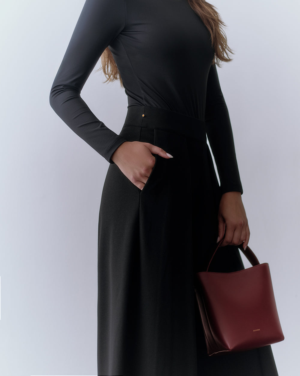 Ponte Pleated Pant Person wearing long-sleeve top and pants, holding a small handbag.