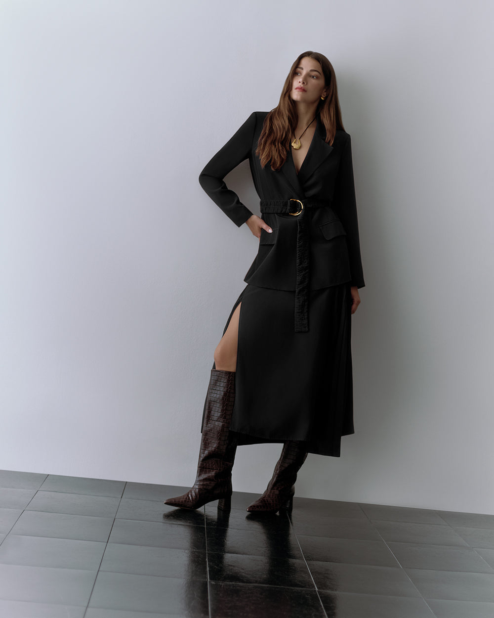 Woman in belted blazer, skirt, croc-embossed leather boots, and necklace.