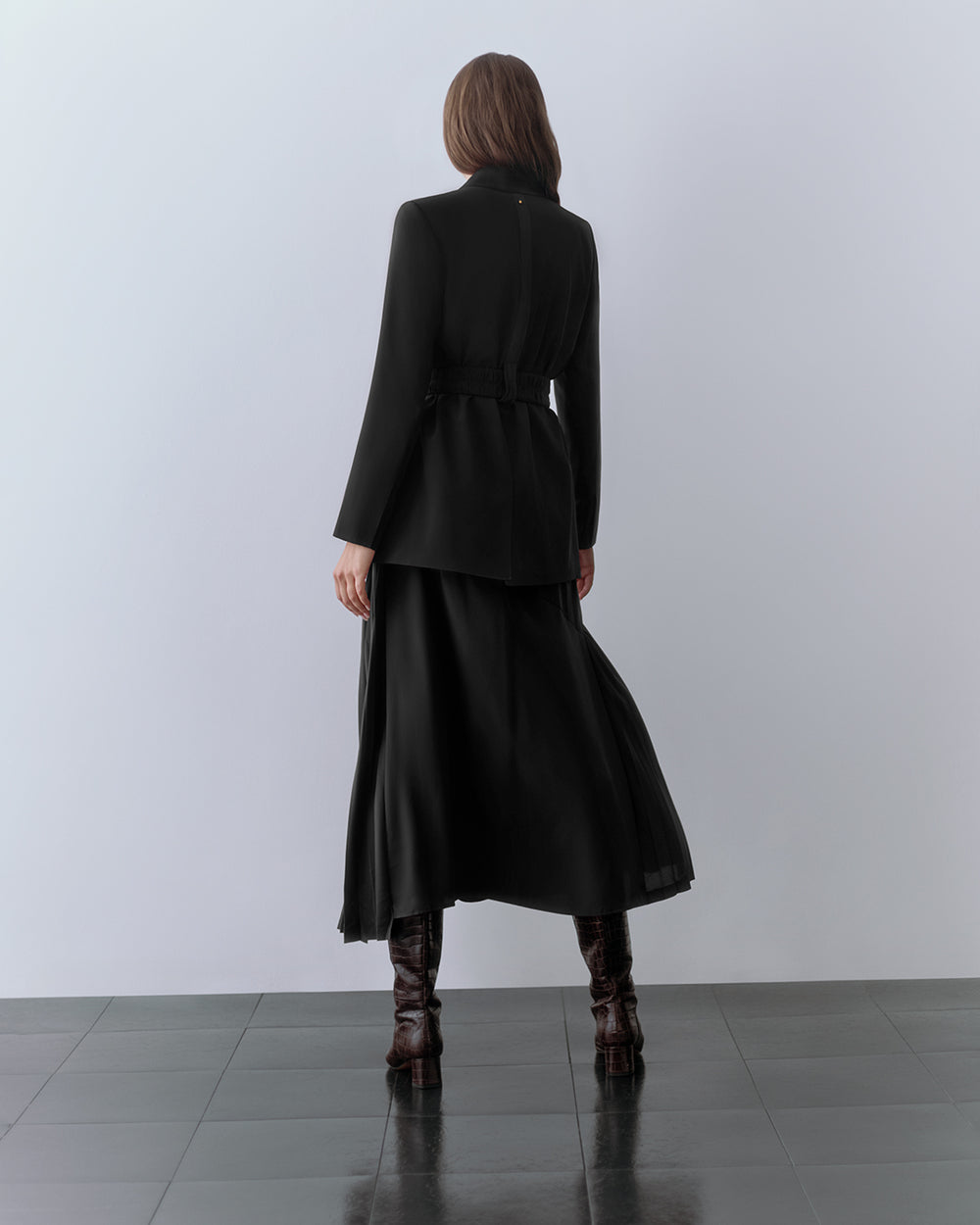 Model wearing blazer, skirt, and boots. standing facing away