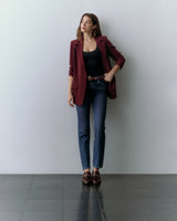 Person stands against a wall, wearing a red blazer, black top, jeans, and loafers.