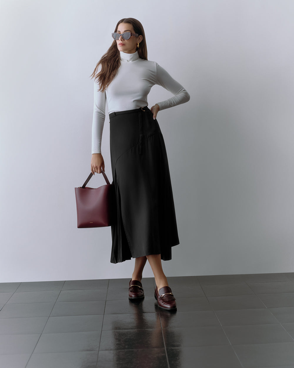 Person wearing a fitted top and long skirt, holding a tote bag and wearing sunglasses.