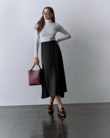 Person wearing a fitted top and long skirt, holding a tote bag and wearing sunglasses.