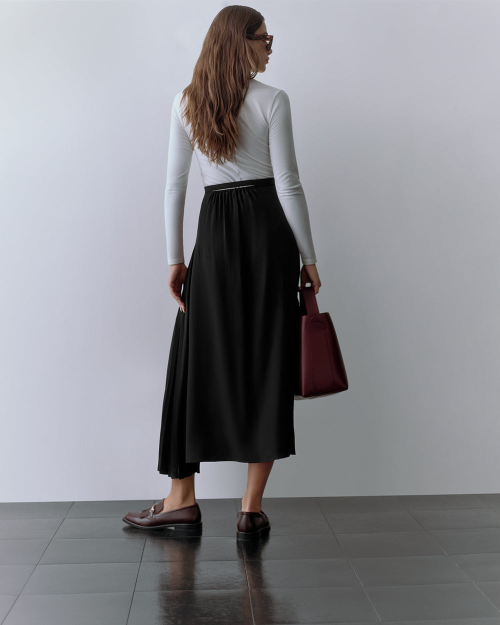 Person with long sleeves and long skirt holding a handbag, facing away from the camera