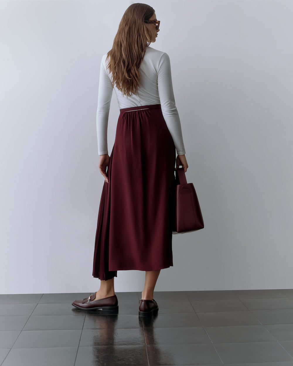 Person with long sleeves and long skirt holding a handbag, facing away from the camera