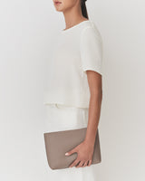 Person holding a clutch bag while wearing a short-sleeve top and pants.