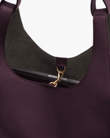 A handbag with an open top and a gold clasp on a strap inside.