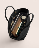 Open handbag containing books, clutch, phone, and drink container