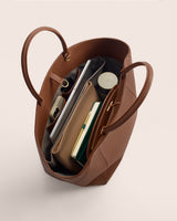 Open tote bag filled with items like books, a pouch, and a bottled container.