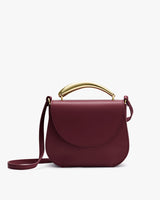 A handbag with a rounded flap, metal handle, and shoulder strap.