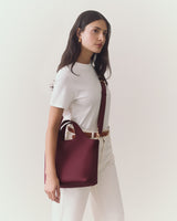 Woman wearing a plain shirt and pants, holding a handbag, with a strap over shoulder.