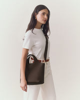 Person in a shirt and pants holding a handbag by the side.