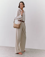 Person standing with a shoulder bag, wearing a shirt and wide pants.