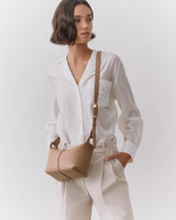 Person wearing a shirt with a shoulder bag and pants hands in pockets