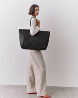 Person standing with a large tote bag over shoulder, wearing long pants and a shirt.