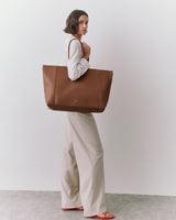 Person holding a large tote bag, standing in a minimalistic setting.