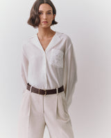 Person wearing a button-up shirt and pleated pants with a belt.