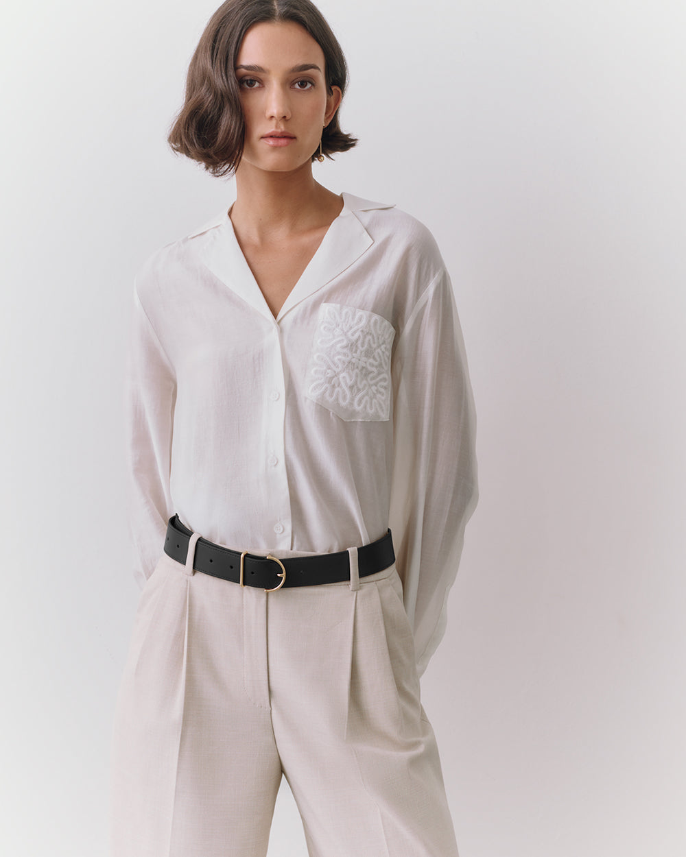 Person wearing a button-up shirt with a patterned pocket and belted trousers.