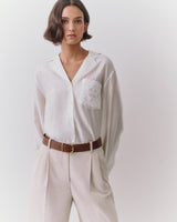 Person wearing a button-up shirt with a pattern on the pocket and belted trousers.