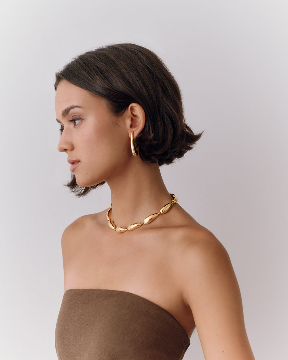 Person wearing hoop earrings and a thick chain necklace, looking to the left.