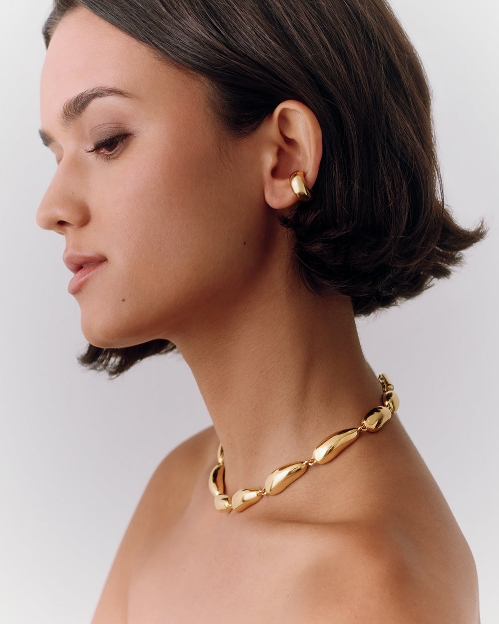 Woman wearing gold necklace and ear cuff looking to the side