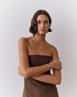 Woman wearing strapless dress, necklace, and bracelet, posing with arms crossed.