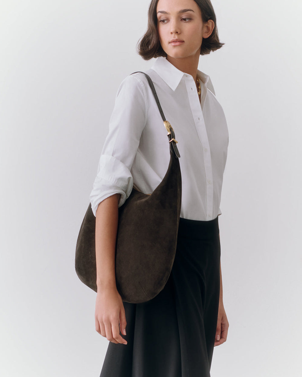 Person wearing a shirt and skirt, holding a shoulder bag.