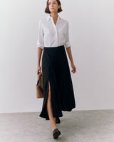 Person wearing a shirt and long skirt holding a handbag.