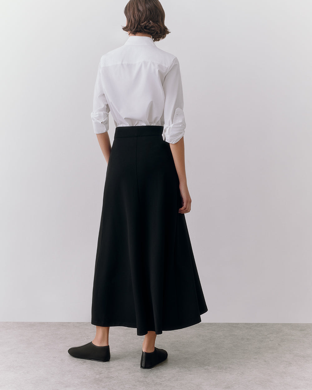 Person in long skirt and shirt standing, rear view.