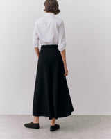 Person in long skirt and shirt standing, rear view.