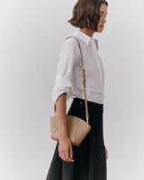 Person in a collared shirt and skirt holding a handbag over their shoulder.