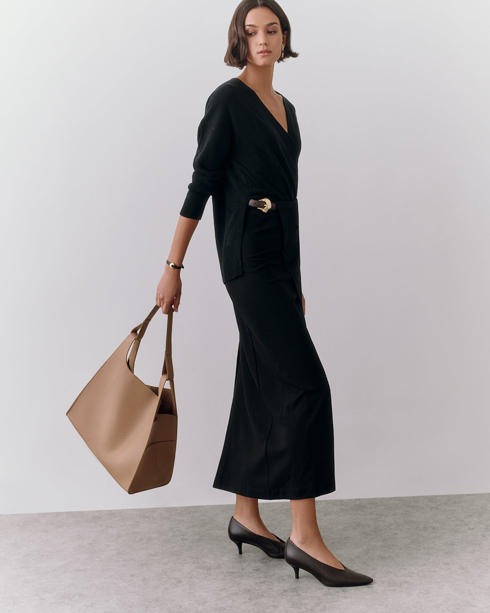 Oversized Double Loop Bag Woman in long dress holds handbag, wearing heels, standing on plain background.