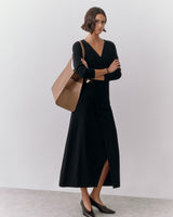 Person wearing a long dress, holding a large bag, standing indoors.