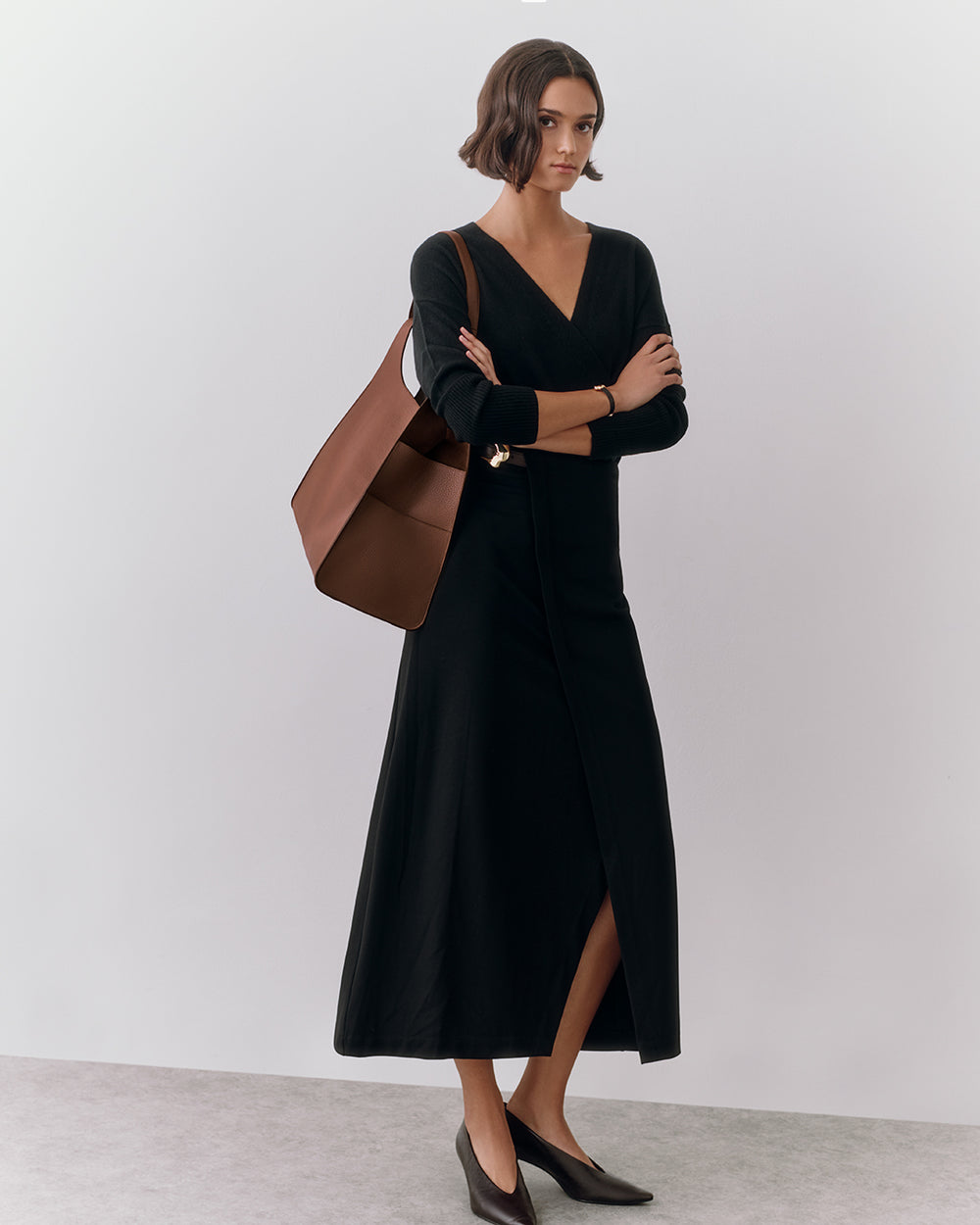 Oversized Double Loop Bag Person in long dress with a large shoulder bag, standing with arms crossed.