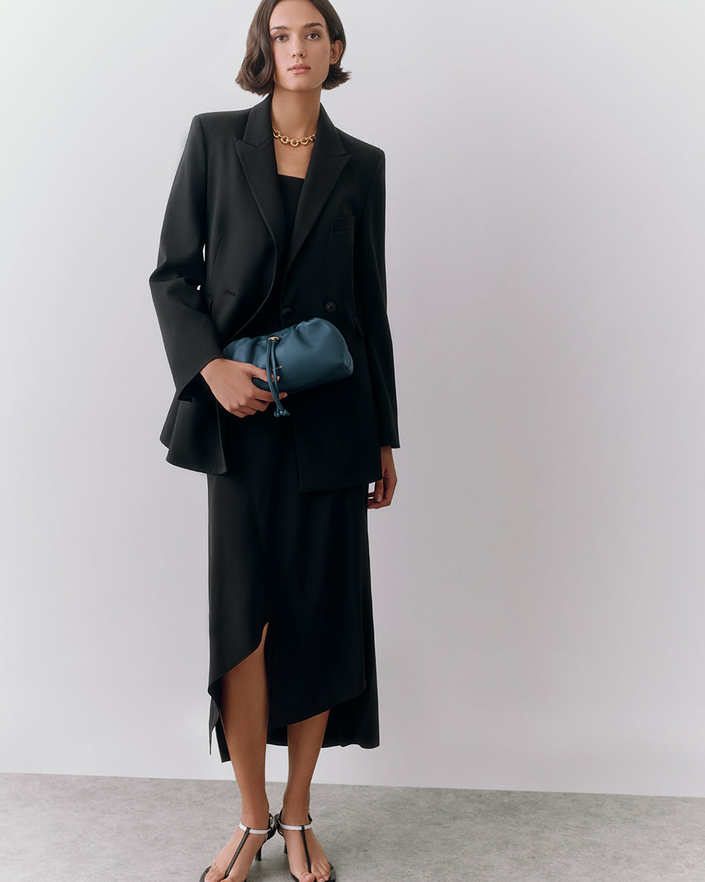 Mini Dia Bag Person in suit holding small bag, wearing sandals and a necklace.