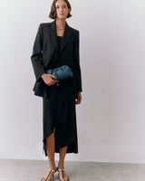 Person in suit holding small bag, wearing sandals and a necklace.