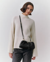 Person wearing a turtleneck sweater and crossbody bag, looking at the camera.