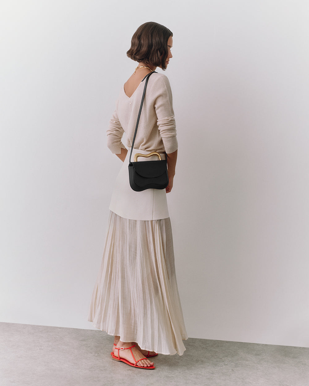 Person standing with crossbody bag and wearing long skirt.