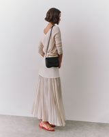 Person standing with crossbody bag and wearing long skirt.
