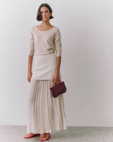 Person wearing a long skirt and sweater, holding a handbag, standing indoors.