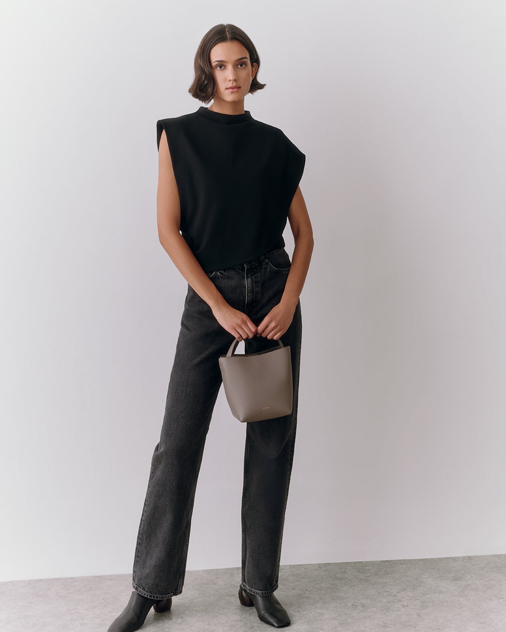 Person wearing a sleeveless top and jeans, holding a small handbag.