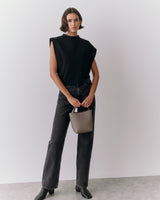 Person wearing a sleeveless top and jeans, holding a small handbag.