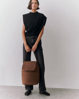 Person standing with backpack, wearing sleeveless top and jeans.